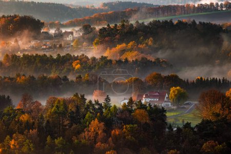 Téléchargez les photos : Saxon, Germany - Warm foggy autumn sunrise above the valley in Saxon Switzerland National park with fresh vivid autumn foliage and fog on the fields - en image libre de droit