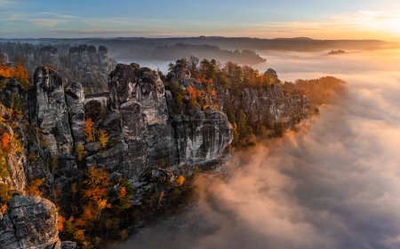 Téléchargez les photos : Saxon, Germany - Aerial panoramic view of the Bastei on a foggy autumn morning with colorful autumn foliage and heavy fog under the rock. Bastei is a rock formation in Saxon Switzerland National Park - en image libre de droit