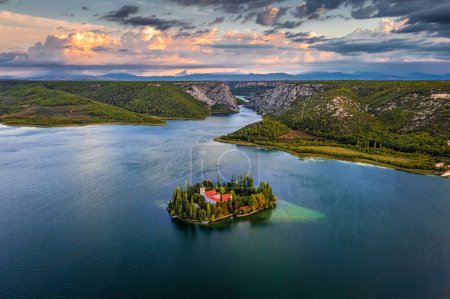 Téléchargez les photos : Visovac, Croatie - Vue aérienne de la belle île du monastère chrétien Visovac dans le parc national de Krka par une matinée d'été avec lever de soleil doré chaud et nuages et eau turquoise claire - en image libre de droit