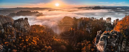 Téléchargez les photos : Saxon, Allemagne - Vue panoramique aérienne du magnifique parc national de la Suisse saxonne près de Dresde par une matinée d'automne brumeuse avec pont Bastei, formation rocheuse et feuillage d'automne doré au lever du soleil - en image libre de droit
