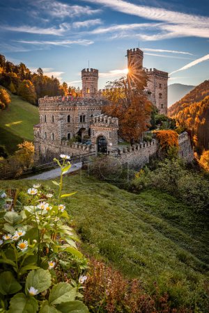 Photo for Latzfons, Italy - Beautiful autumn scenery at Gernstein Castle (Castello di Gernstein, Schloss Gernstein) at sunrise in South Tyrol with blue sky and golden foliage and flowers at foreground - Royalty Free Image