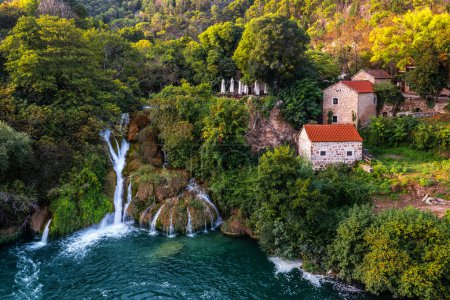 Foto de Krka, Croacia - Vista aérea de las hermosas cascadas de Krka en el Parque Nacional Krka en una brillante mañana de verano con casitas tradicionales y follaje verde y agua turquesa - Imagen libre de derechos