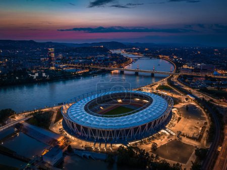 Photo for Budapest, Hungary - Aerial skyline of Budapest at dusk, including illuminated National Athletics Centre, Rakoczi bridge over River Danube and new skyscraper building at background with colorful sunset sky - Royalty Free Image