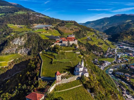 Téléchargez les photos : Klausen, Italie - Vue aérienne de l'abbaye de Saben (Monastero di Sabiona) avec Chiusa (Klausen) commune au nord-est de la ville de Bolzano et du Tyrol du Sud Dolomites en arrière-plan par une journée d'été ensoleillée - en image libre de droit
