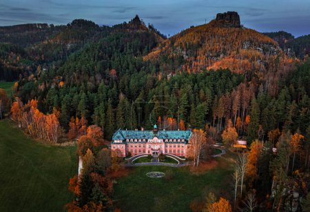 Foto de Jetrichovice, República Checa - Vista aérea de la hermosa mansión rosa cerca de Jetrichovice al atardecer en un día de otoño con el mirador de Mariina vyhlidka al fondo y folige de otoño en la región de Suiza bohemia - Imagen libre de derechos
