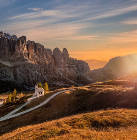 Foto de South Tyrol, Italy - The Chapel of San Maurizio (Cappella Di San Maurizio) at the Passo Gardena Pass in the Italian Dolomites at autumn with warm colorful sunset sky and clouds - Imagen libre de derechos