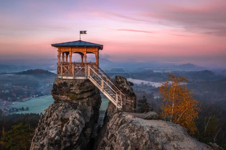 Jetrichovice, Czech Republic - Aerial view of Mariina Vyhlidka (Mary's view) lookout with foggy Czech autumn landscape, golden foliage and colorful pink sunrise sky in Bohemian Switzerland National Park