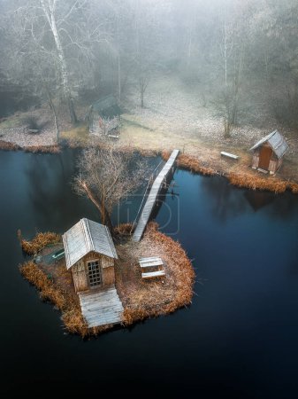 Photo for Szodliget, Hungary - Aerial view of a dreamy winter scene at Szodliget fishing lake with small island, fishing huts and heavy fog on a cold winter morning - Royalty Free Image