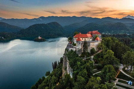 Téléchargez les photos : Bled, Slovénie - Vue panoramique aérienne du magnifique château de Bled (Blejski Grad) avec le lac de Bled (Blejsko Jezero), l'église de l'Assomption de Maria et le coucher de soleil coloré sur les Alpes juliennes en arrière-plan - en image libre de droit