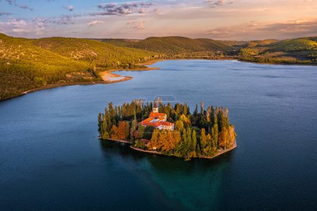 Téléchargez les photos : Visovac, Croatie - Vue aérienne de l "île du monastère chrétien Visovac dans le parc national de Krka par une matinée ensoleillée d'automne avec lever de soleil doré, feuillage d'automne coloré et eau bleu turquoise clair - en image libre de droit