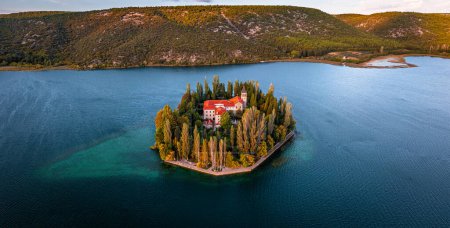 Foto de Visovac, Croacia - Vista panorámica aérea de la isla del monasterio cristiano de Visovac en el Parque Nacional Krka en una soleada mañana de otoño con amanecer dorado, follaje de otoño colorido y agua azul turquesa clara - Imagen libre de derechos
