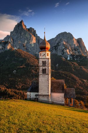 Photo for Seis am Schlern, Italy - Famous St. Valentin Church and Mount Sciliar mountain at background. Idyllic mountain scenery in the Italian Dolomites with blue sky and warm sunlight at South Tyrol at sunset - Royalty Free Image