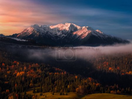 Foto de Eslovaquia - Vista aérea de otoño de los picos de las montañas de los Altos Tatras en el parque nacional al amanecer con colorido follaje otoñal, niebla y dramático cielo dorado - Imagen libre de derechos