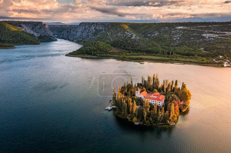 Foto de Visovac, Croatia - Aerial view of Visovac Christian monastery island in Krka National Park on a sunny autumn morning with dramatic golden sunrise and clouds and clear turquoise blue water - Imagen libre de derechos