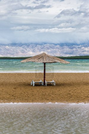Photo for Nin, Croatia - Reed sunshade at the empty Queen's Beach by the mediterranean town of Nin at the end of summer with Velebit Mountains at background and turquoise Adriatic sea water at autumn time - Royalty Free Image