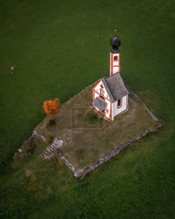 Val Di Funes, Dolomites, Italy - Aerial view of the beautiful St. Johann Church (Chiesetta di San Giovanni in Ranui) at South Tyrol with green grass, cow and autumn foliage