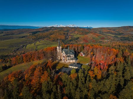 Levoca, Slovaquie - Vue aérienne de la basilique de la Visitation de la Bienheureuse Vierge Marie par une journée ensoleillée d'automne avec un feuillage d'automne coloré. Hautes montagnes Tatras et ciel bleu clair à l'arrière-plan