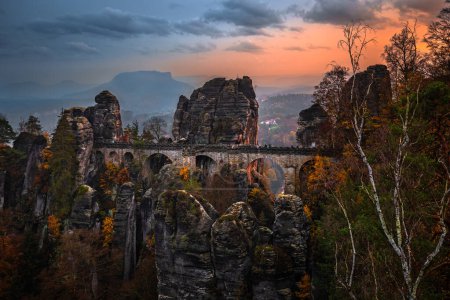 Foto de Sajón, Alemania - El puente Bastei con un soleado atardecer otoñal con colorido follaje y cielo. Bastei es famoso por la hermosa formación rocosa en el Parque Nacional Sajón Suiza cerca de Dresde - Imagen libre de derechos