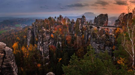Téléchargez les photos : Saxon, Allemagne - Vue panoramique sur le pont Bastei avec un coucher de soleil ensoleillé d'automne au feuillage coloré et au ciel. Bastei est célèbre pour la belle formation rocheuse dans le parc national suisse de Saxe près de Dresde - en image libre de droit