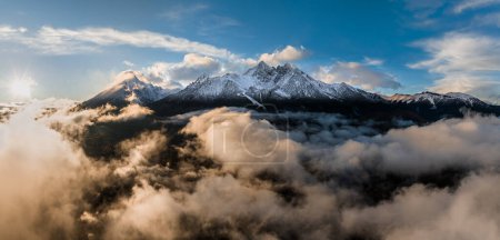 Téléchargez les photos : Tatranska Lomnica, Slovaquie - Vue panoramique aérienne des sommets enneigés des Hautes Tatras au-dessus des nuages avec le Pic Lomnicky, le deuxième plus haut sommet des Hautes Tatras au coucher du soleil - en image libre de droit