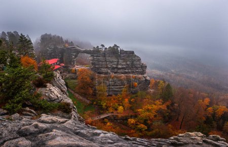 Hrensko, Czech Republic - Panoramic view of the famous Pravcicka Archway (Pravcicka Brana) in Bohemian Switzerland National Park, the biggest natural arch in Europe on a foggy day with colorful autumn foliage
