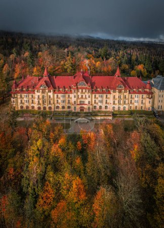 Tatrzanska Lomnica, Slovakia - Aerial view of beautiful warm colorful forest at a hotel by the High Tatras with golden autumn foliage and foggy mountains at background at sunset