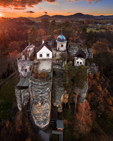 Foto de Sloup v Cechach, República Checa - Vista aérea del Castillo de Rock Sloup en el norte de Bohemia con una espectacular puesta de sol colorida, nubes, cielo azul y follaje de otoño - Imagen libre de derechos