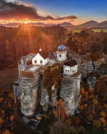 Sloup v Cechach, Tschechische Republik - Luftaufnahme der Felsenburg Sloup in Nordböhmen mit einem dramatischen bunten Sonnenuntergang, Wolken, blauem Himmel und Herbstlaub