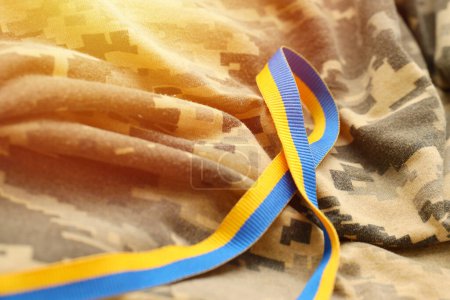 Pixeled digital military camouflage fabric with ribbon in blue and yellow colors. Attributes of ukrainian patriotic soldier uniform