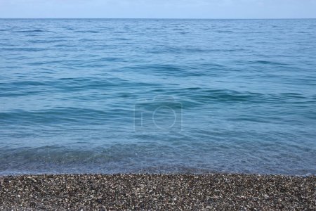 Bank of pebbles with the sea and beach in the background. Pebbles and water on the sea shore in Kemer, Antalya in Turkey