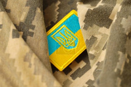 Pixeled digital military camouflage fabric with ukrainian flag and coat of arms on chevron in blue and yellow colors. Attributes of ukrainian soldier uniform