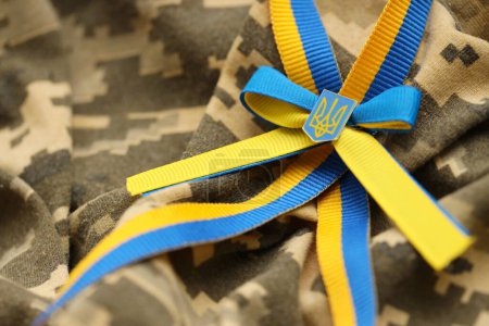 Pixeled digital military camouflage fabric with ukrainian flag and coat of arms on stripes ribbon in blue and yellow colors. Attributes of ukrainian soldier uniform