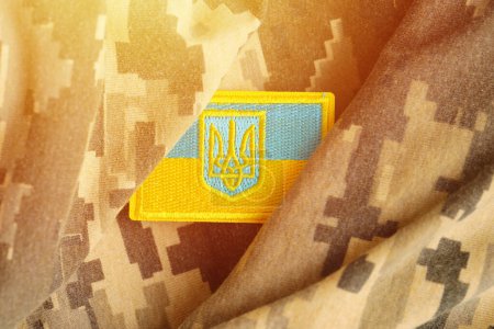 Photo for Pixeled digital military camouflage fabric with ukrainian flag and coat of arms on chevron in blue and yellow colors. Attributes of ukrainian soldier uniform - Royalty Free Image