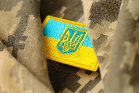 Tela de camuflaje militar digital pixelada con bandera ucraniana y escudo de armas en chevron en colores azul y amarillo. Atributos del uniforme de soldado ucraniano