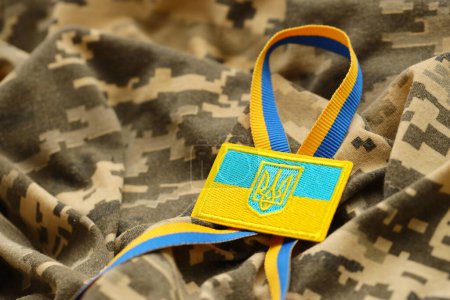 Pixeled digital military camouflage fabric with ukrainian flag and coat of arms on chevron in blue and yellow colors. Attributes of ukrainian soldier uniform