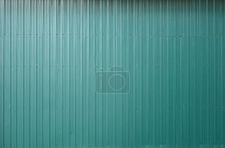 Siding metal vertical panels texture closeup in the daytime outdoors. Metal wall or fence embossed metal sheets. Terrain and large metal sheet as a barrier or fence