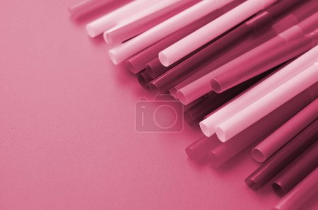 Many colorful straws for drinks lies on a bright orange background surface Image toned in Viva Magenta, color of the 2023 year