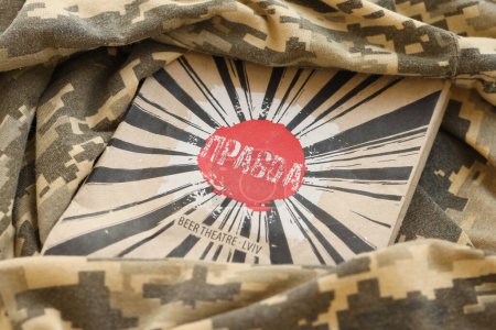 Foto de KYIV, UKRAINE - MAY 4, 2022 Logo of Pravda patriotic Ukrainian beverage company on cardboard pack among military camouflage fabric - Imagen libre de derechos