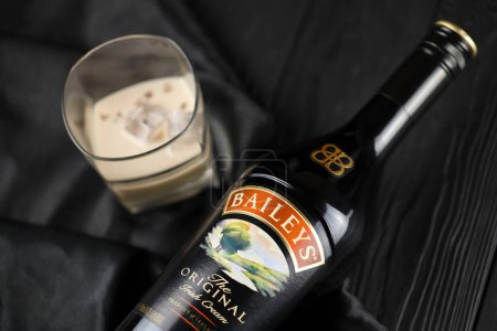 Foto de KYIV, UKRAINE - MAY 4, 2022 Baileys original alcohol bottle on wooden table with black fabric on background. Elite alcohol production - Imagen libre de derechos