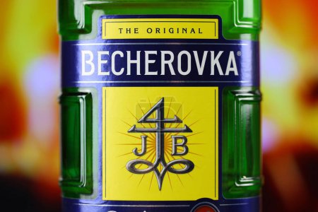 Photo for KYIV, UKRAINE - MAY 4, 2022 Becherovka original alcohol bottle on wooden table with red fireplace on background. Elite alcohol production - Royalty Free Image