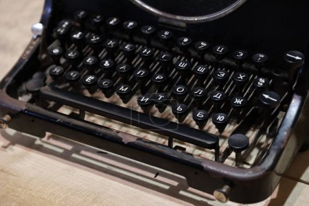 Téléchargez les photos : Détails d'une vieille machine à écrire rétro de style vintage avec des surfaces poussiéreuses sur une table en bois à l'intérieur sombre - en image libre de droit