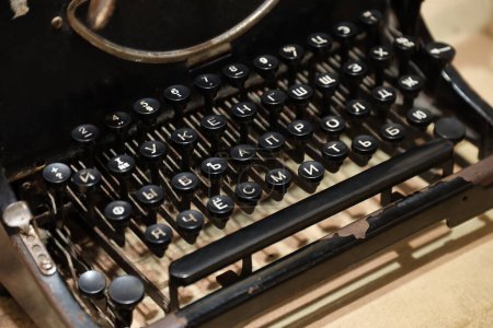 Téléchargez les photos : Détails d'une vieille machine à écrire rétro de style vintage avec des surfaces poussiéreuses sur une table en bois à l'intérieur sombre - en image libre de droit
