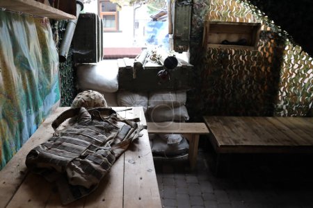 Foto de Un casco militar de un soldado ucraniano con un pesado chaleco antibalas sobre una mesa de madera en el interior del puesto de control - Imagen libre de derechos