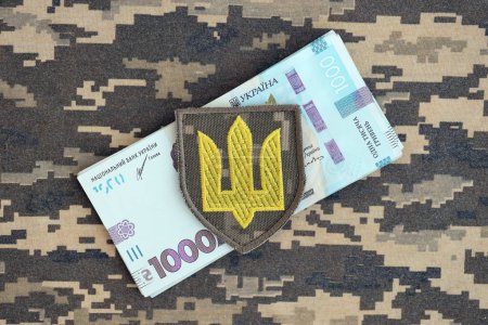 Symbole de l'armée ukrainienne et tas de projets de loi hryvnia sur l'uniforme militaire. Paiements aux soldats de l'armée ukrainienne, salaires aux militaires. Guerre en Ukraine