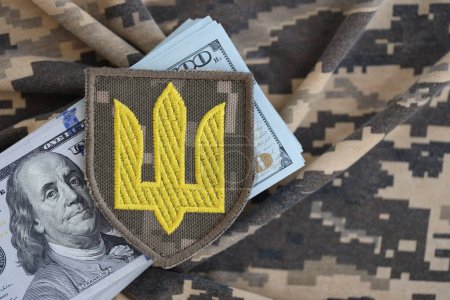 Téléchargez les photos : Symbole de l'armée ukrainienne et des billets en dollars sur l'uniforme militaire. Paiements aux soldats de l'armée ukrainienne des États-Unis, salaires aux militaires. Soutien de guerre à l'Ukraine - en image libre de droit