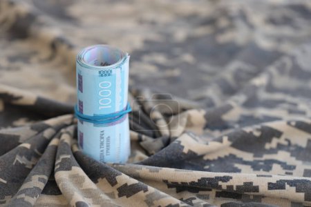 Ukrainian hryvnia bills on fabric with texture of Ukrainian military pixeled camouflage. Cloth with camo pattern in grey, brown and green pixel shapes. Official uniform of Ukrainian soldiers close up