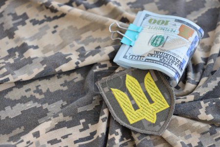 Téléchargez les photos : Symbole de l'armée ukrainienne et des billets en dollars sur l'uniforme militaire. Paiements aux soldats de l'armée ukrainienne des États-Unis, salaires aux militaires. Soutien de guerre à l'Ukraine - en image libre de droit
