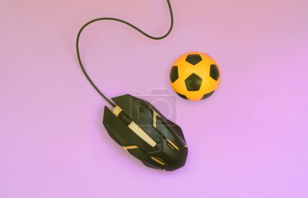 Téléchargez les photos : Ballon de football avec souris d'ordinateur sur fond violet. Concept de jeux vidéo, eSports, paris sportifs et jeux de hasard en ligne - en image libre de droit