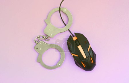 Photo for Computer mouse in a red color is chained in handcuffs on the background of purple color. The concept of combating computer crime, hackers and piracy. Flat lay top view - Royalty Free Image