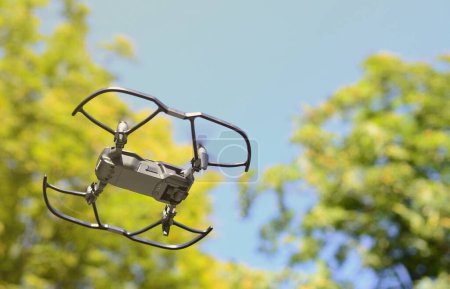 Photo for Small UAV drone copter with digital camera is flying near the green trees in daytime - Royalty Free Image